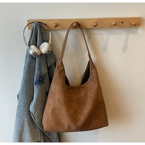 Detailed close-up of brown PU leather tote bag with vertical stitching on wooden hanger