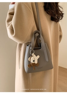 Dettaglio borsa a secchiello grigia in pelle con ciondolo a orso su sfondo cappotto beige