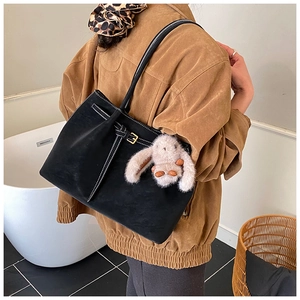 Detail of black suede tote bag with white contrast stitching and plush rabbit charm
