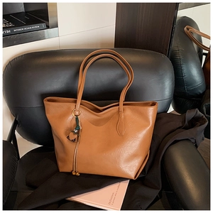 Close-up detail of the brown faux leather texture and tassel charm on a large tote bag