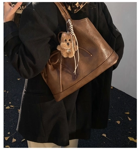 Close-up of a brown leather tote bag with a cute plush dog charm on a street