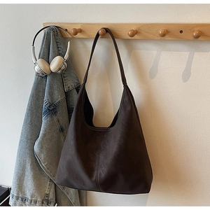 Detail of a large brown hobo tote bag hanging on wooden hooks with casual lifestyle items