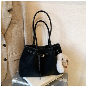 Detail of black leather tote bag with white contrast stitching and a fluffy rabbit charm