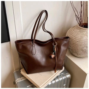 Detail of vintage brown leather tote bag with unique tassel charm on travel luggage