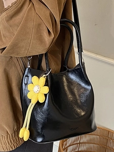 Glossy black leather bucket bag with yellow daisy charm and stylish shoulder strap design