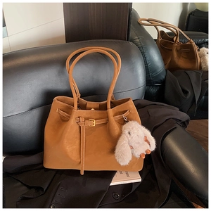 Detail view of a caramel brown tote bag with slim buckle and plush rabbit charm