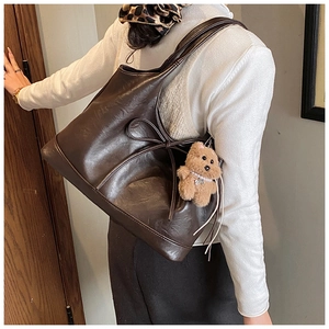 Detail of deep brown tote bag featuring leather bow and plush bear charm accessory