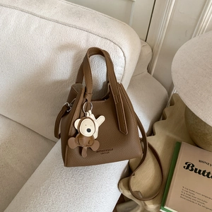Dettaglio borsa a secchiello marrone con grana litchi, logo e ciondolo a forma di orso