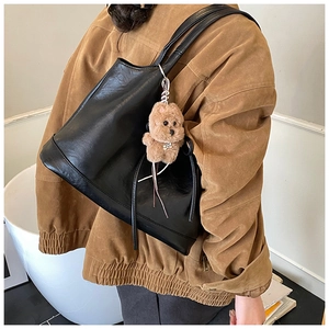 Detailed view of black leather tote bag with a cute plush dog charm on shoulder