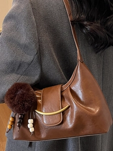 Brown faux leather shoulder bag with gold crescent buckle and fuzzy pompom charm