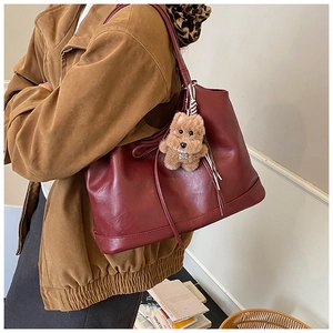 Detailed side view of a large burgundy tote bag with brown plush pendant accessory