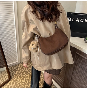 Detail of a brown suede moon hobo bag with a cute plush bear charm on a model's shoulder