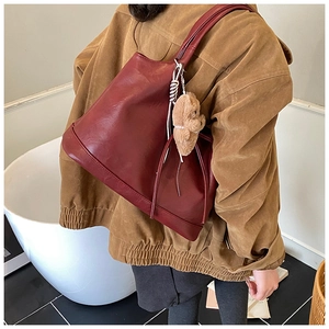 Close-up of burgundy leather tote bag with a brown plush bear charm for winter fashion
