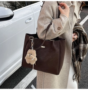 Detail of dark brown large tote bag with soft plush charm in an outdoor fashion setting