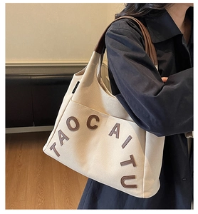 Close-up of cream canvas tote bag featuring brown leather handles and TAOCAITU letter patch
