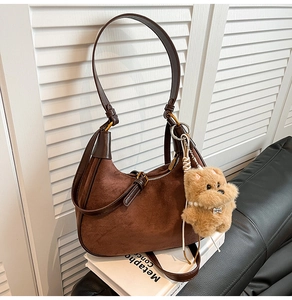 Detail of dark brown suede half-moon bag with gold zipper and a cute teddy bear charm