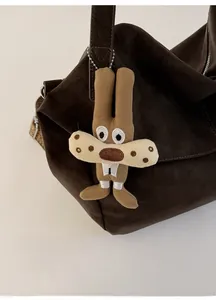 Close-up of a cute brown plush cartoon charm with silver bead chain on a suede tote bag