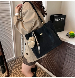 Detail of black leather tote bag with gold metal logo and brown plush bear charm