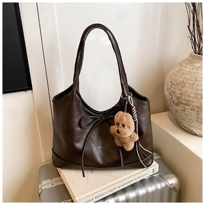 Detailed view of brown leather tote bag with bow tie and plush puppy charm