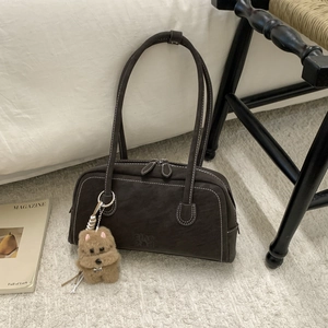 Detailed close-up of dark brown bowling bag with white stitching and plush dog charm