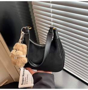 Detail of black suede hobo bag with leather trim and brown plush bear charm