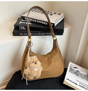 Detail of brown suede crescent hobo bag featuring a plush dog charm and long leather strap