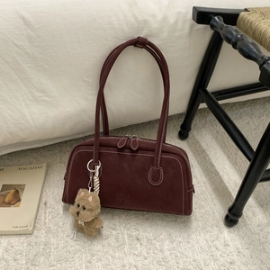 Detail of burgundy suede bowling bag featuring contrast stitching and plush puppy charm