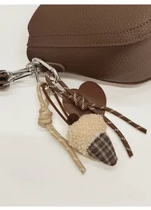 Close-up of acorn charm with MOMENT leather tag and braided ropes on brown bag
