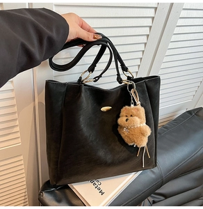 Detail of black leather tote bag with gold metal buckle and cute teddy bear pendant charm