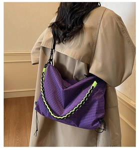Detailed view of large purple checkered tote bag with neon braided straps on a trench coat