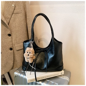 Detail of black PU leather tote bag with bow decoration and plush dog charm on luggage