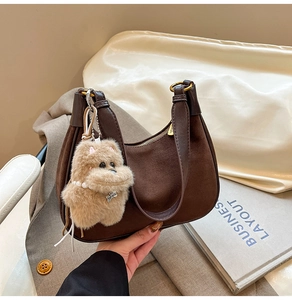 Detail of suede hobo bag with leather handle and cute plush charm in dark brown color