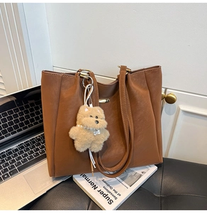 Detail of a brown PU leather tote bag with a plush bear charm on an office desk