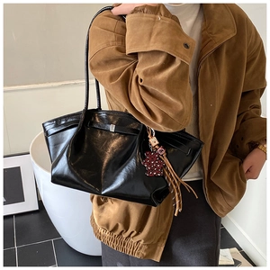 Fashionable black glossy patent leather tote bag with bear charm on model's shoulder