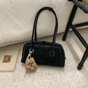 Detail of black suede shoulder bag featuring white contrast stitching and plush dog charm