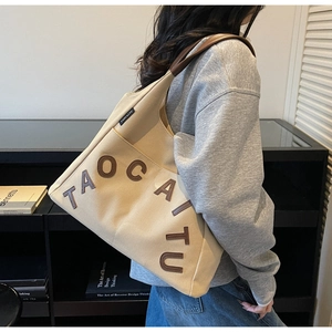 Detail of beige canvas tote with brown leather handles and 3D textured lettering