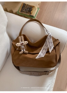 Brown oversized tote bag with silk scarf and plush charm on a white cozy sofa