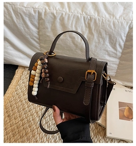 Détail d'un sac bandoulière rétro marron chocolat avec un pendentif en perles de bois