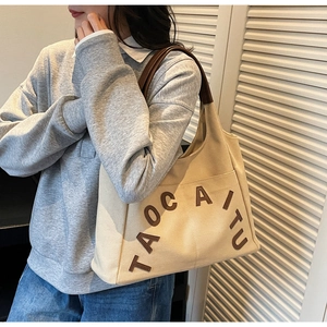 Detail of beige canvas tote bag featuring brown leather handles and TAOCAITU lettering
