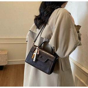 Détail d'un sac bandoulière en cuir marron foncé avec accessoire de perles colorées