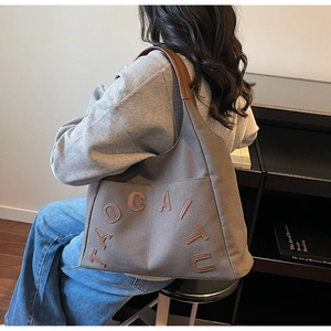 Detail view of canvas tote bag with brown leather handles and TAOCAITU logo lettering