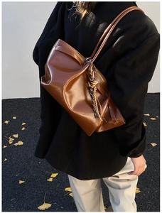 Detail of a brown glossy leather shoulder bag with pleated design in an autumn setting