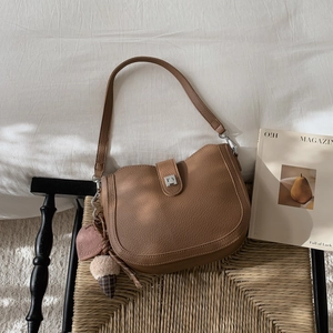 Detail of brown litchi leather shoulder bag with silver buckle and plush heart charm