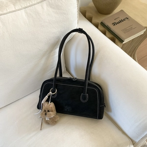 Detail of black matte Boston bag with white stitching and plush puppy pendant on sofa