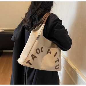 Detail view of beige canvas tote bag with brown leather handles and brand letter patch