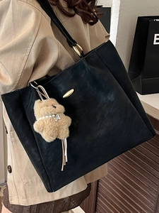 Large black leather tote bag with gold hardware and plush bear charm worn by a model