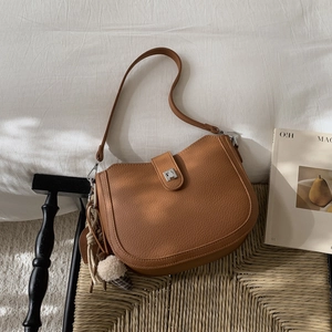 Close-up of brown pebbled leather bucket bag with silver buckle and plush ball charm