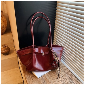 Detail of burgundy glossy tote bag with heart charm on a wooden table setup