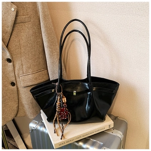 Macro detail of glossy black tote bag featuring metallic buckle and decorative tassel charm