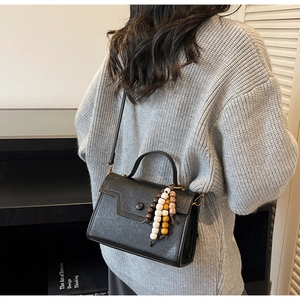 Détail du sac bandoulière noir avec franges en bois et boucle métal sur pull gris